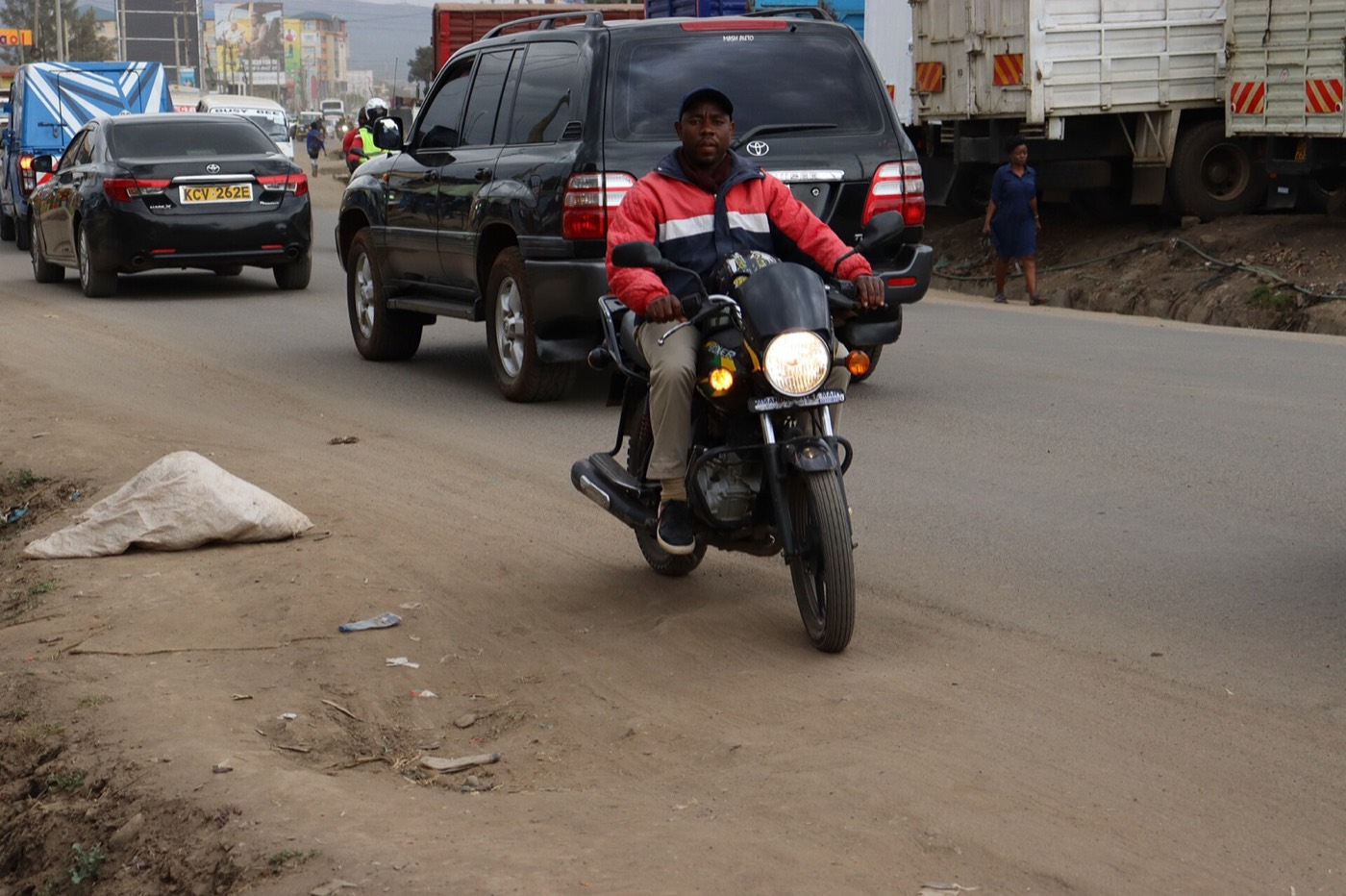 A boda boda rider carrying a passenger on a Kenyan road