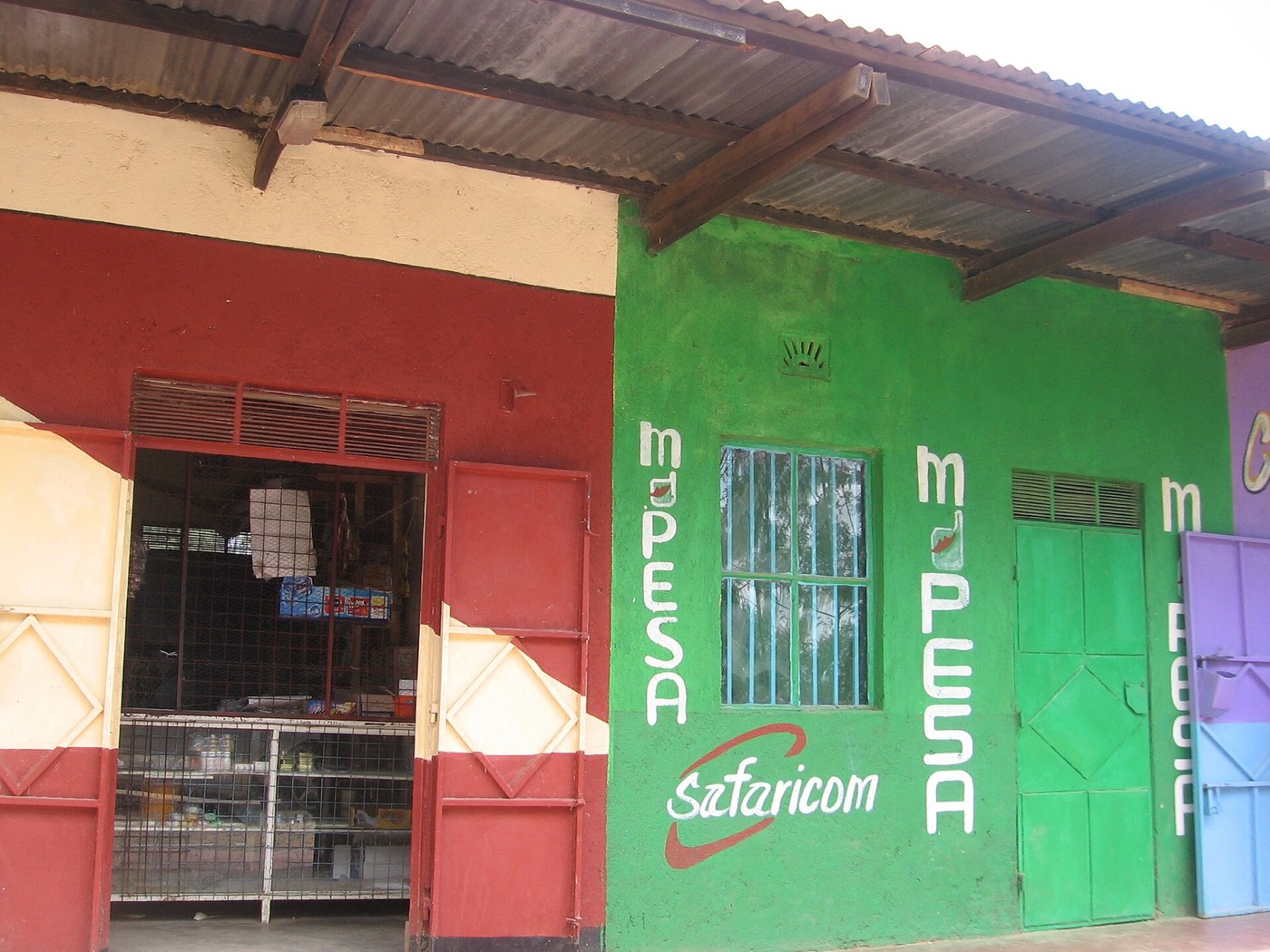 A green M-Pesa kiosk at a roadside shopping row